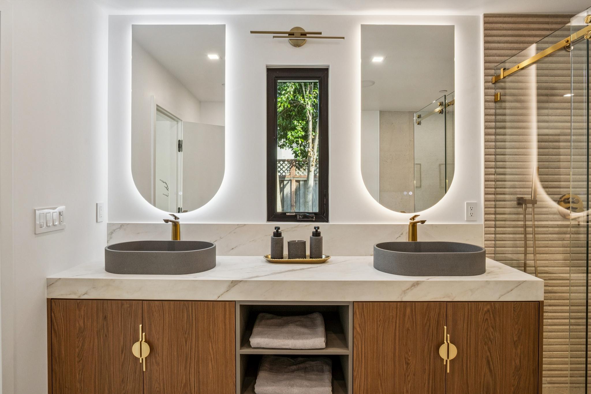 Luxury custom bathroom design in Willow Glen, San Jose, featuring a dual-sink floating walnut vanity, custom backlit arched mirrors, concrete vessel sinks, and brushed gold fixtures built by Ritz Builders.