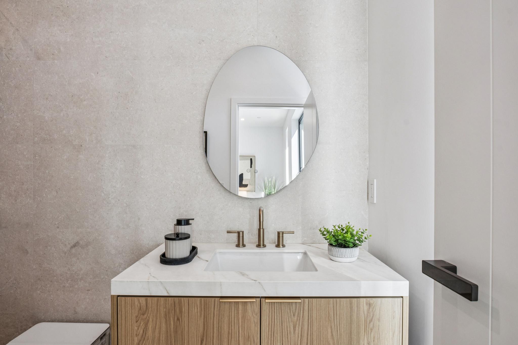 Minimalist luxury bathroom in Willow Glen, San Jose, highlighting a custom organic asymmetrical mirror, wall-mounted bronze plumbing fixtures, and a floating fluted wood vanity built by Ritz Builders.
