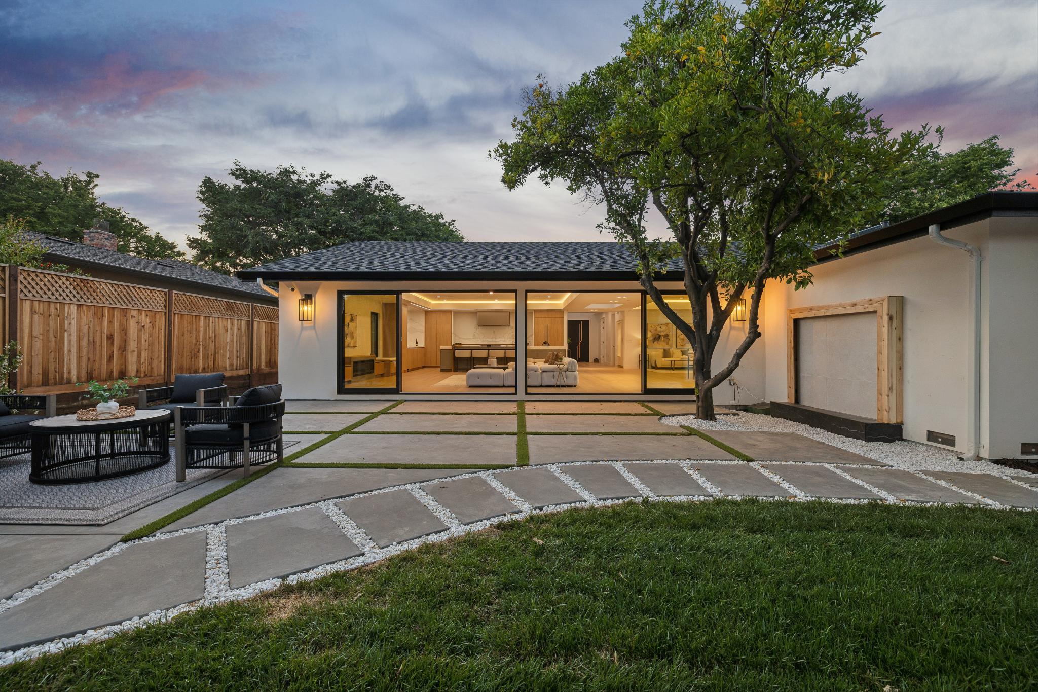 Rear twilight elevation of a modern farmhouse custom home in Willow Glen, highlighting seamless open-concept architecture, premium landscape hardscaping, and a fully illuminated luxury great room built by Ritz Builders.