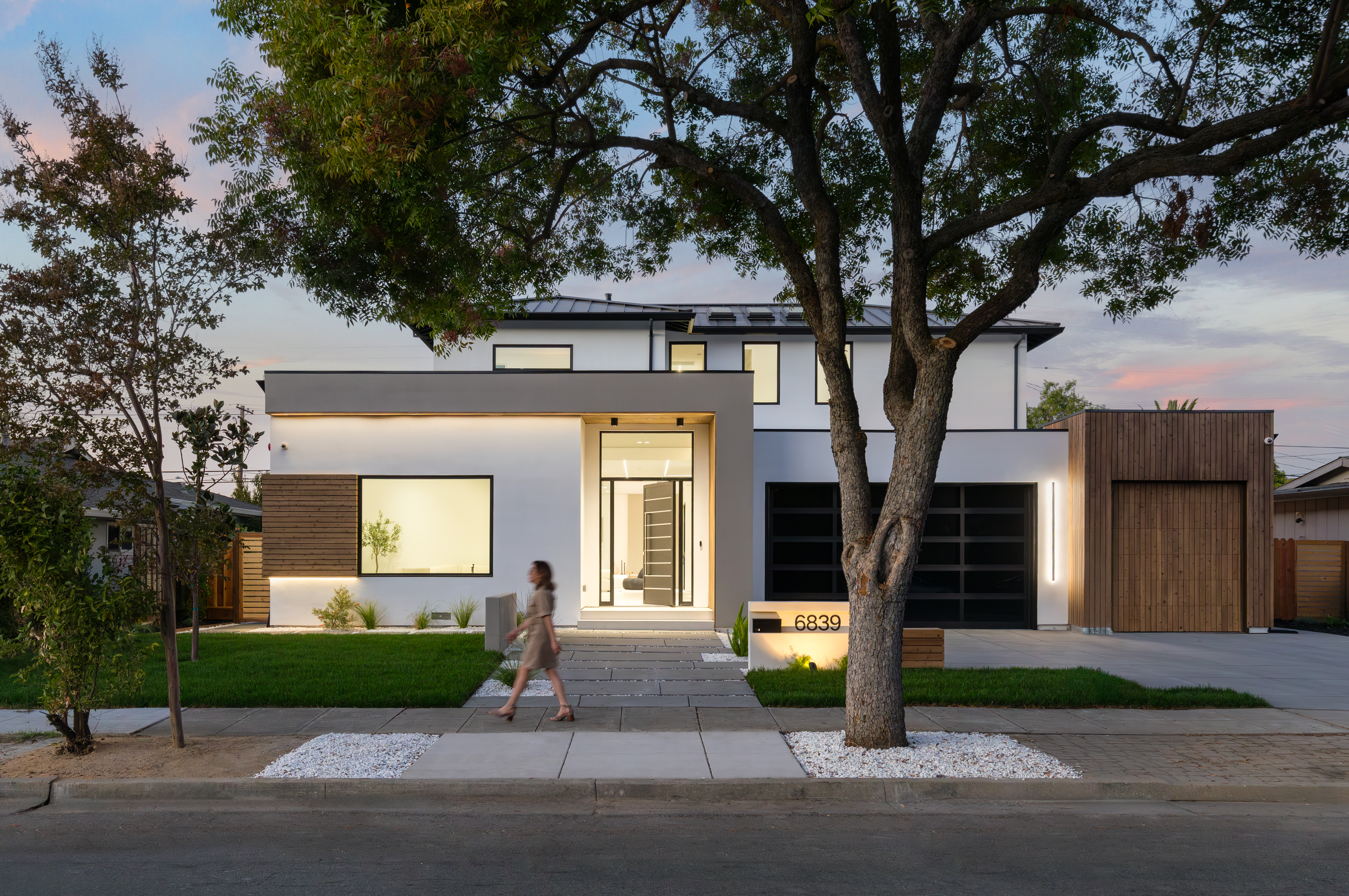 Homeowner walking toward a modern, newly constructed Bay Area custom home featuring white stucco and custom wood garage cladding.